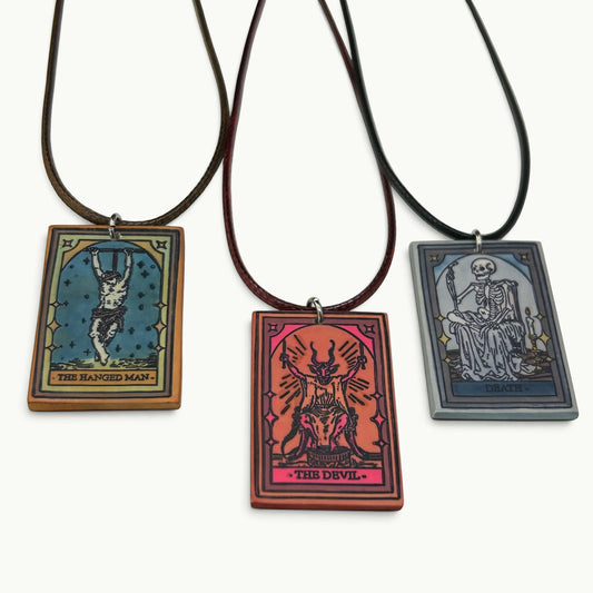 DTB Alchemy trio of handmade matte white polymer clay tarot card pendant necklaces featuring The Devil, Hanged Man, and Death designs with hand-stained ink finishes on adjustable cords.